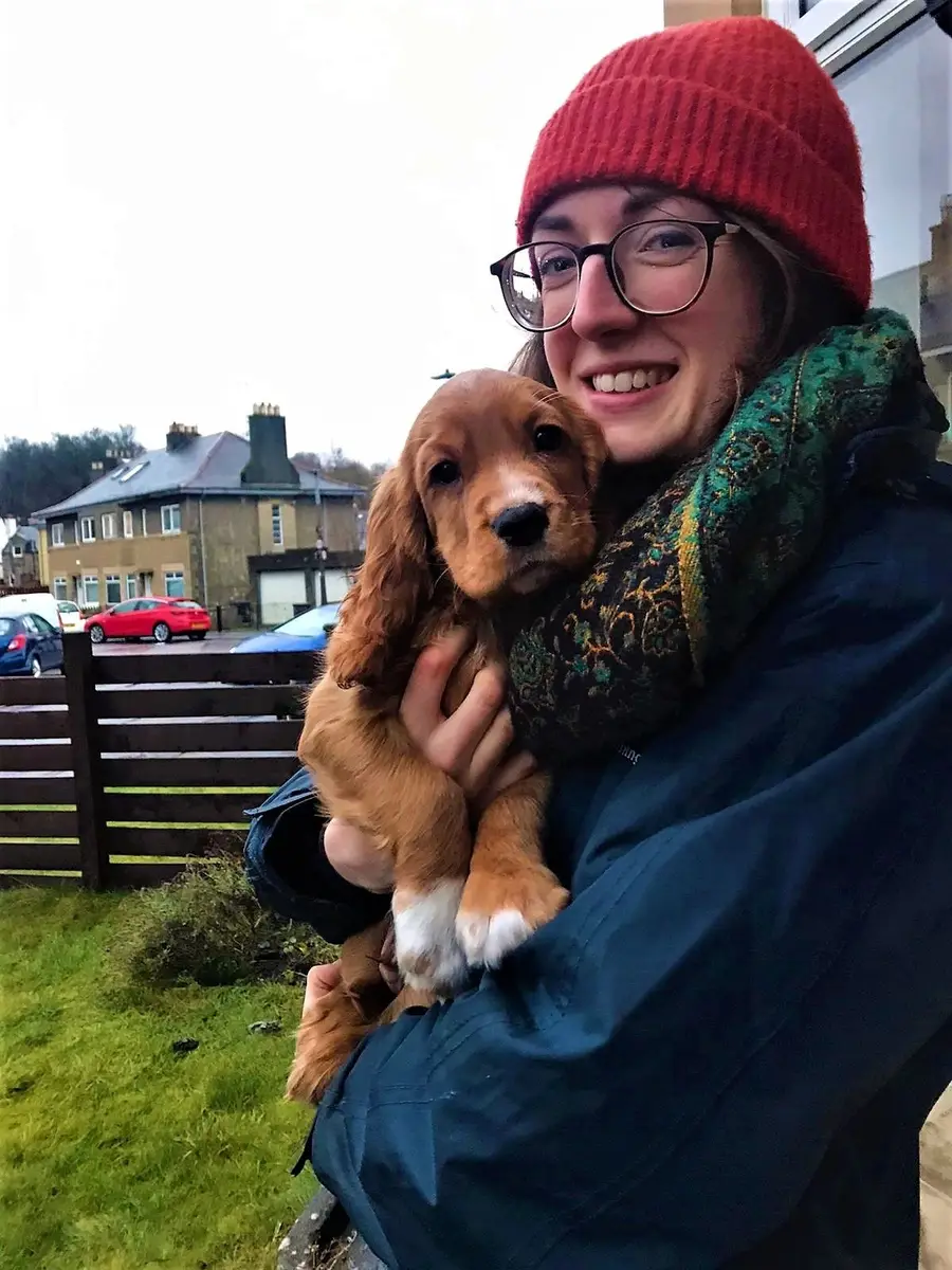 Rosy in a red hat holding a cocker spaniel puppy