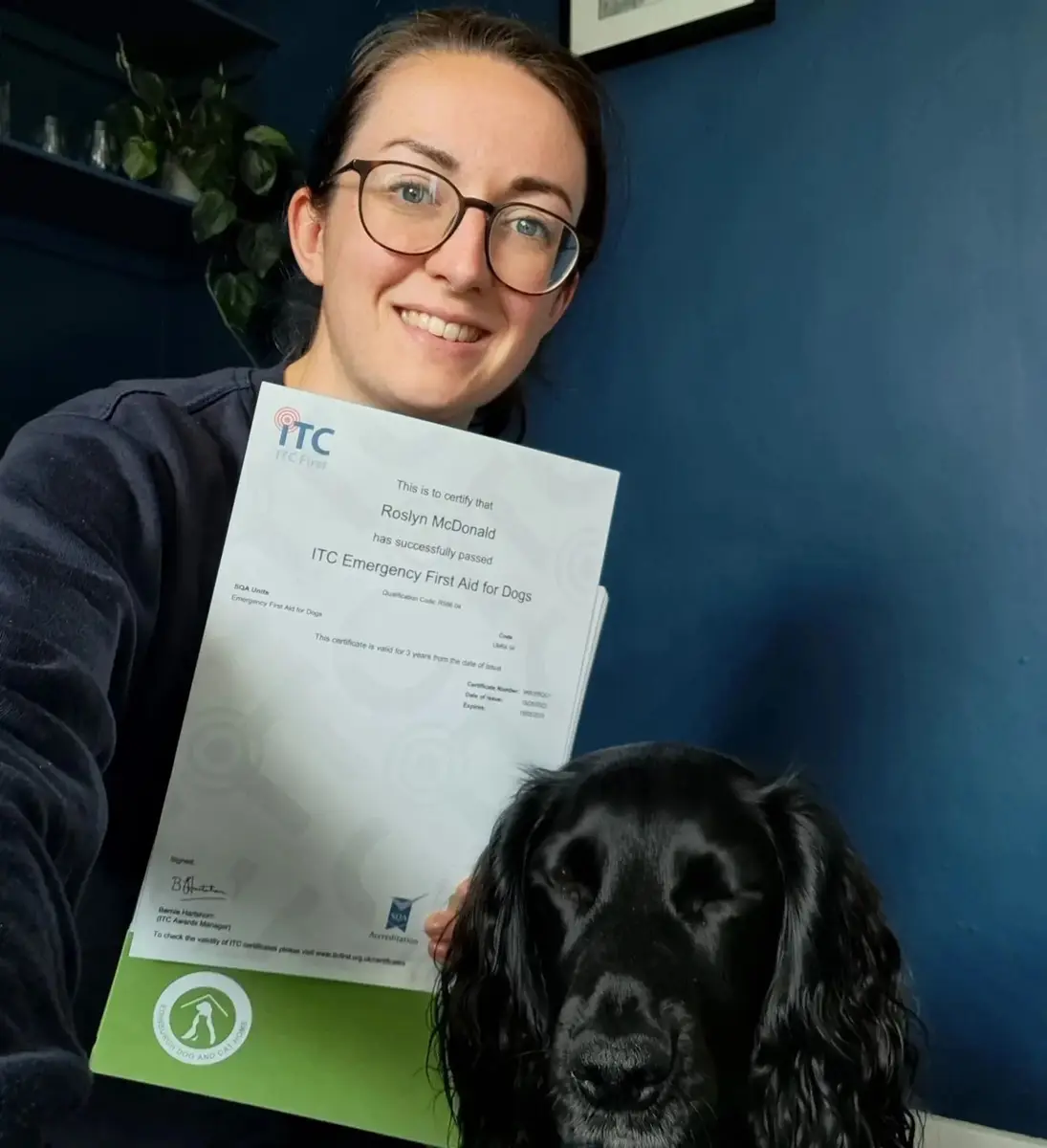Rosy holding her canine first aid certificate beside her black spaniel