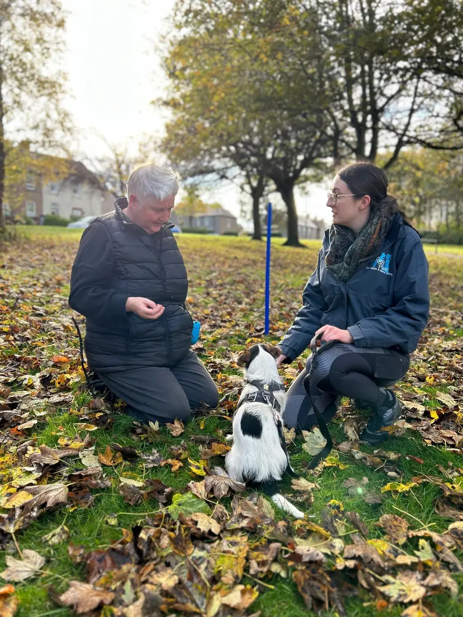 Rosy and a client kneeling with a black and white dog among autumn leaves